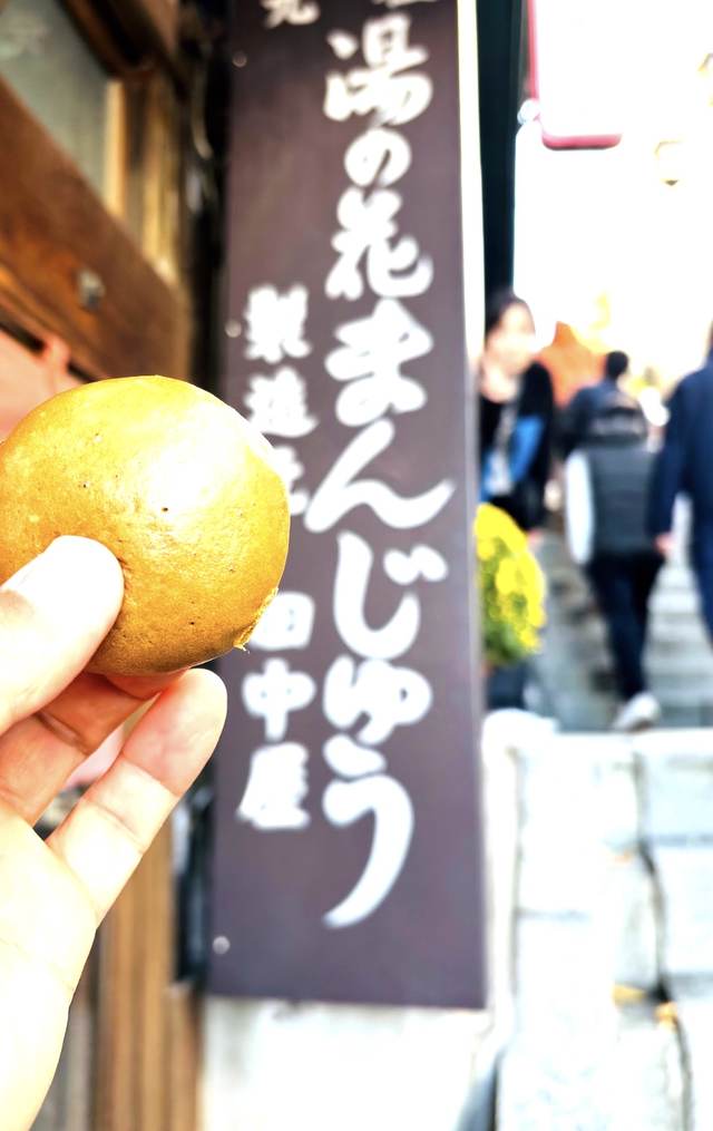 手に持った湯の花まんじゅうと店の看板